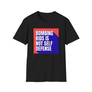 May include: Black t-shirt with the text "BOMBING KIDS IS NOT SELF DEFENSE" in white, set against a red and blue background. The shirt is a classic crew neck style.