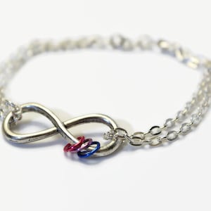 May include: A silver infinity symbol charm bracelet with a double chain and a charm of three small rings in pink, blue, and red.