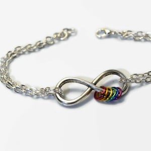 May include: A silver infinity symbol charm bracelet with a rainbow of coloured rings attached to the centre. The bracelet is made of a double chain.