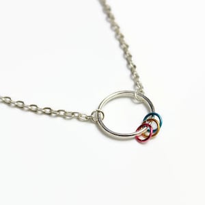 May include: A silver chain necklace with a silver circle pendant. The circle pendant has four smaller colourful rings attached to it. The rings are teal, pink, red, and gold.