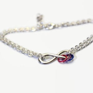 May include: A silver infinity charm bracelet with a red, blue, and purple charm. The bracelet is made of a delicate chain.