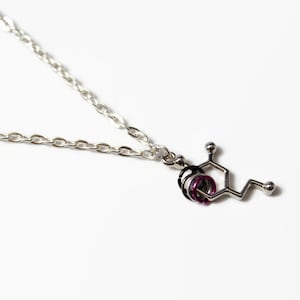 May include: A silver chain necklace with a silver pendant shaped like a chemical molecule. The pendant has purple accents.