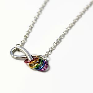 Peut inclure: Un collier avec un symbole infini argenté et un groupe d'anneaux de couleur arc-en-ciel attachés au bas.