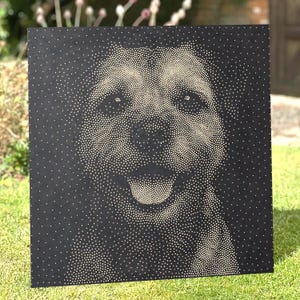 May include: A square black panel featuring a pointillist portrait of a dog created with numerous small white dots. The dog is depicted facing forward with its mouth open in a happy expression, with the dots varying in density to form the image.