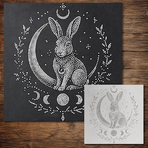 May include: A square stencil featuring a dot-art design of a rabbit sitting on a crescent moon, surrounded by a circular wreath of leaves and stars. Below the moon, a series of lunar phases are depicted in a dot pattern on a dark background.
