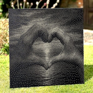 May include: A square black panel featuring a pointillist design created with numerous small white dots. The arrangement of these dots forms the negative space image of two hands positioned together to create a heart shape in the center.