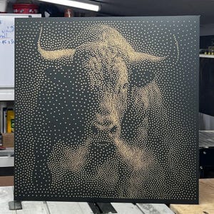 May include: A black square canvas with a bull's head design created using small, light-coloured dots in a pointillism style. The bull's horns are visible, and the dots give a textured appearance.