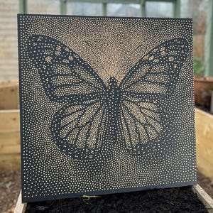 Könnte beinhalten: Ein quadratisches, schwarzes Kunstwerk mit einem Schmetterlingsdesign. Der Schmetterling wird mit kleinen, hellfarbigen Punkten vor dem dunklen Hintergrund erstellt. Das Kunstwerk wird in einem Holzrahmen präsentiert.