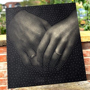 May include: A square black wall art piece featuring a pointillist design created with small white dots. The pattern depicts two hands reaching towards each other, with the dots varying in density to form the shape of the fingers and palms.