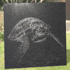 May include: A square black metal panel featuring a perforated design that forms the silhouette of a sea turtle. The image is created by numerous small circular holes of varying density, allowing light to pass through the dark surface.