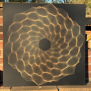 Puede incluir: Una pieza de arte mural cuadrada y negra con un diseño geométrico. La obra de arte muestra un patrón circular compuesto por líneas doradas interconectadas, creando una ilusión óptica fascinante. El centro del diseño es un vacío circular oscuro.