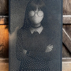 Può includere: Un'opera d'arte rettangolare nera con un ritratto creato con punti bianchi. I punti variano in dimensioni e densità, creando un effetto in scala di grigi che delinea i tratti della figura, tra cui un papillon e una mano che tiene un oggetto.