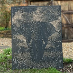 May include: A rectangular black metal panel featuring a pointillist-style elephant silhouette created with numerous small, light-colored dots. The design depicts the head and ears of an elephant against a background of scattered, cloud-like dot patterns.
