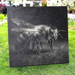 Könnte beinhalten: Eine quadratische schwarze Platte mit einem Punktmalerei-Design einer Biene in Weiß. Das Bild des Insekts wird vollständig durch unterschiedliche Dichten kleiner weißer Punkte auf dem dunklen Hintergrund erzeugt, die Flügel, Körper und Fühler bilden.