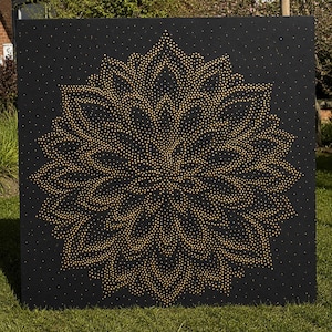 May include: A square black panel featuring a large, intricate mandala pattern created with numerous small, metallic gold studs. The design radiates from the center with symmetrical, petal-like shapes, covering the majority of the dark surface.
