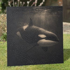 May include: A square black art panel featuring a stippled illustration of an orca whale created with numerous small tan dots. The dots vary in density to form the shape of the orca, with the highest concentration of dots highlighting the whale's dorsal fin, eye patch, and body contours against the dark background.