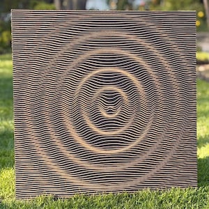 Puede incluir: Arte mural cuadrado de madera con fondo negro y un patrón de líneas onduladas paralelas en color marrón claro. Las líneas crean un efecto circular tridimensional en el centro de la obra de arte. El arte se exhibe sobre hierba verde.