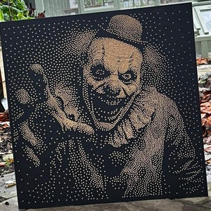 May include: A black canvas features a menacing clown portrait created with small, gold-colored dots. The clown wears a top hat and a ruffled collar, with a sinister grin. The artwork is square and appears to be displayed indoors.
