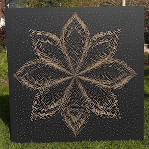 May include: A square black panel featuring a large, symmetrical lotus flower design created with numerous small, gold-colored dots. The dots are densely arranged to form the petals, with a lighter scattering of dots across the background.