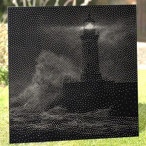 May include: A square black metal panel featuring a pointillist design created by numerous small circular perforations. The arrangement of these holes forms the distinct silhouette of a lighthouse emitting a beam of light over a dark sea.