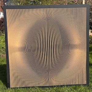 Puede incluir: Una obra de arte mural cuadrada de madera con marco negro. La obra presenta líneas verticales y paralelas en color marrón claro que se curvan hacia adentro, creando un efecto tridimensional. El fondo es un degradado de marrón claro.