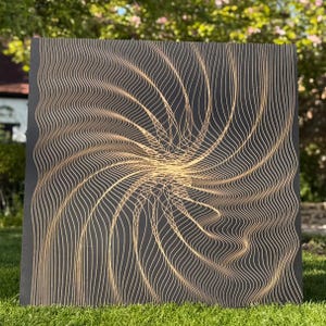 May include: A square, black wooden wall art piece with a gold, swirling, wave-like design. The artwork features a central spiral that radiates outward, creating a dynamic and textured visual effect. The piece is displayed on green grass.