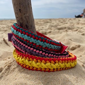 Peut inclure: Trois colliers en paracorde tressée empilés. Le collier supérieur présente des brins bleu sarcelle, rouges et vert foncé. Le collier central est violet, rose et noir. Le collier inférieur est jaune, orange et rouge. Chaque collier a une boucle.