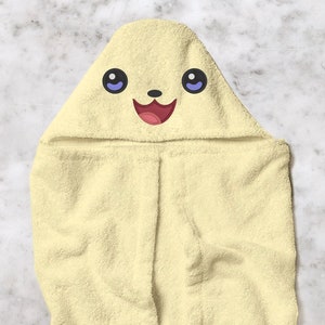 May include: A light yellow hooded baby towel with a smiling cartoon face embroidered on the hood. The face has large black eyes with purple pupils, a black nose, and a red open mouth. The towel is made of soft terry cloth.