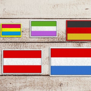 Puede incluir: Cinco parches bordados sobre un fondo de madera blanco. Los parches son rectangulares y presentan las banderas de Austria, Alemania, los Países Bajos, la bandera del orgullo pansexual y la bandera del orgullo genderqueer.