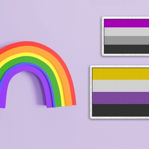 May include: Two embroidered patches on a purple background. The top patch is a purple, white, and gray flag. The bottom patch is a yellow, white, and purple flag.