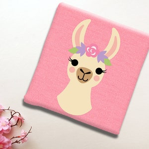 May include: A pink t-shirt with a cartoon llama wearing a flower crown. The llama has a light brown face with black eyes and a pink nose.