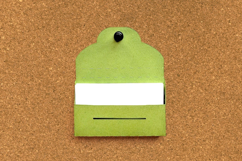 May include: A green card with a white rectangle in the center, pinned to a corkboard. The card has a rounded top and a black push pin.