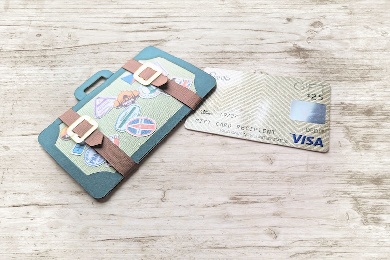 May include: A green suitcase with brown straps and a gift card with the text "GIFT CARD RECIPIENT" and the Visa logo. The gift card has a balance of &pound;125.