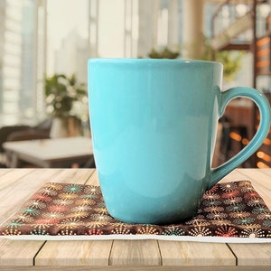 May include: A blue ceramic mug with a handle sits on a brown and white patterned coaster. The coaster is on a wooden table.