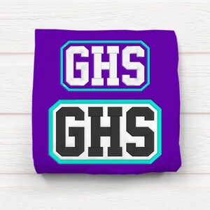 May include: Purple t-shirt with two white and black patches that say "GHS" in a bold font.