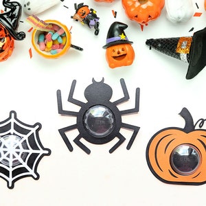 Könnte beinhalten: Halloween-Dekorationen, darunter eine schwarze Spinne, ein Spinnennetz und ein Kürbis mit einem durchsichtigen Fenster. Die Dekorationen befinden sich auf einem weißen Hintergrund.