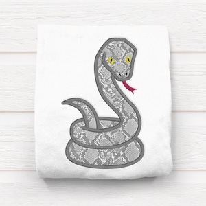 May include: A gray snake with a patterned skin and yellow eyes is embroidered on a white background. The snake is curled up with its head raised and its tongue sticking out.