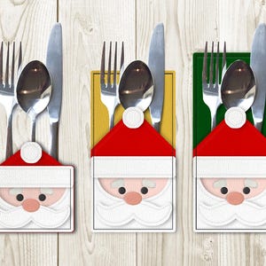 May include: Three Santa Claus themed place card holders for silverware. Each holder is made of felt and features a red Santa hat, white beard, and black eyes. The holders are in front of a wood background.