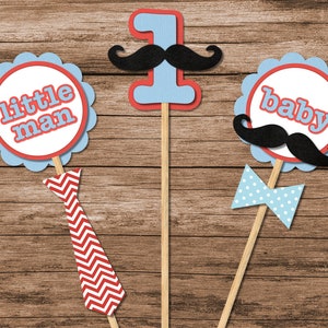 May include: Three blue and red paper party props with sticks. The first prop has a red and white chevron tie, the second prop has a blue number one with a black moustache, and the third prop has a blue bow tie with white polka dots and a black moustache. The props say "little man", "1", and "baby".