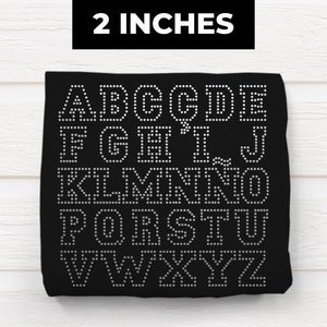 May include: Black fabric with the alphabet A-Z in white outlined with small white dots. The fabric is 2 inches wide.