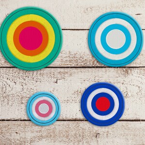 Op de afbeelding: Vier ronde onderzetters met concentrische ringen in verschillende kleuren. Eén onderzetter heeft een turquoise rand met gele, oranje en roze ringen. Een andere heeft een blauwe rand met witte en lichtblauwe ringen.