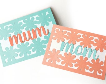 May include: Two cards with a floral design and the words "mum" and "mom" in different colors. The card with "mum" is light blue with a coral colored word, and the card with "mom" is coral with a light blue word.