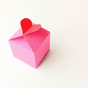 Puede incluir: Una caja de regalo rosa con lunares blancos y una tapa en forma de corazón rojo.