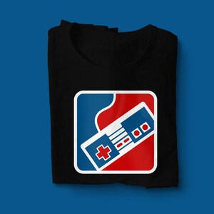 Op de afbeelding: Een zwart t-shirt met een wit, blauw en rood logo met een retro-videogamescontroller. Het logo heeft de vorm van een sportteamlogo.