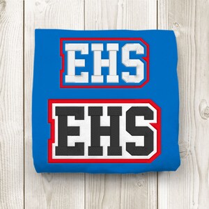 Puede incluir: Una camiseta azul con dos parches blancos y rojos con bordes que dicen "EHS" en letras blancas y negras.