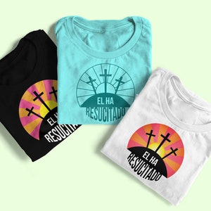 May include: Three folded t-shirts with a graphic design of three crosses on a hill with a sunrise behind them. The text "EL HA RESUCITADO" is below the crosses. The shirts are black, white, and light blue.