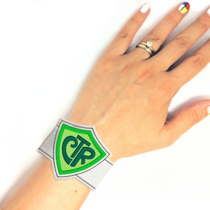 May include: A white wristband with a green shield-shaped patch featuring the letters "CTR" in green.