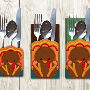 May include: Three brown and orange turkey-shaped utensil holders with a green, brown, and orange design. Each holder has a fork, knife, and spoon inside.