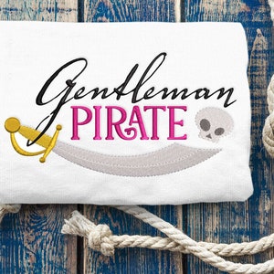 May include: White fabric with embroidered text "Gentleman Pirate" in black and pink lettering. A gold and white embroidered sword and a skull are also embroidered on the fabric.