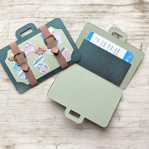 May include: A green and brown paper craft suitcase with a ticket pocket and a handle. The suitcase is decorated with travel stickers and has a brown leather strap.